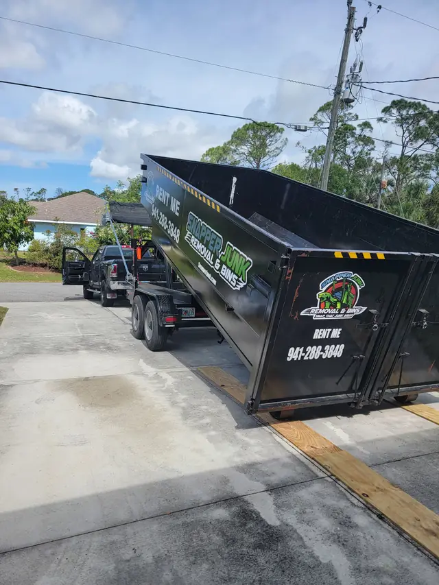 A Snapper roll-off tilted up on a tandem trailer behind a black pickup on a Florida street